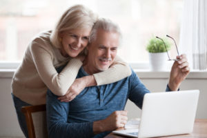 a man with Parkinson's at home on his laptop with his wife next to him