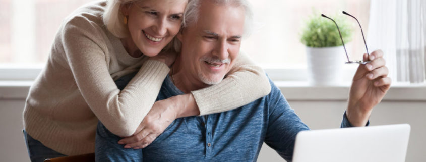 a man with Parkinson's at home on his laptop with his wife next to him