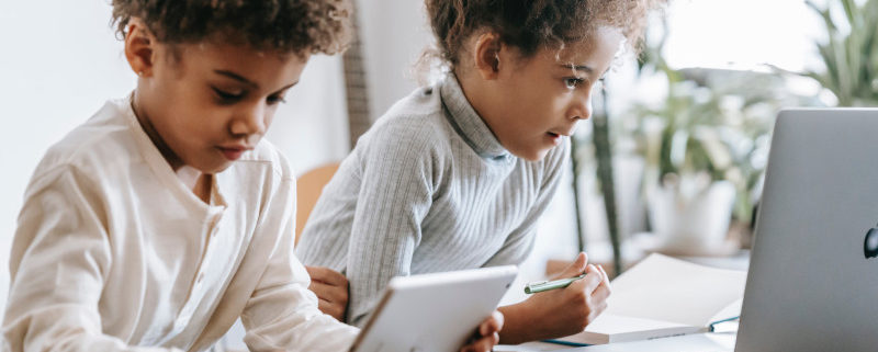 two children on laptops from home doing summer school