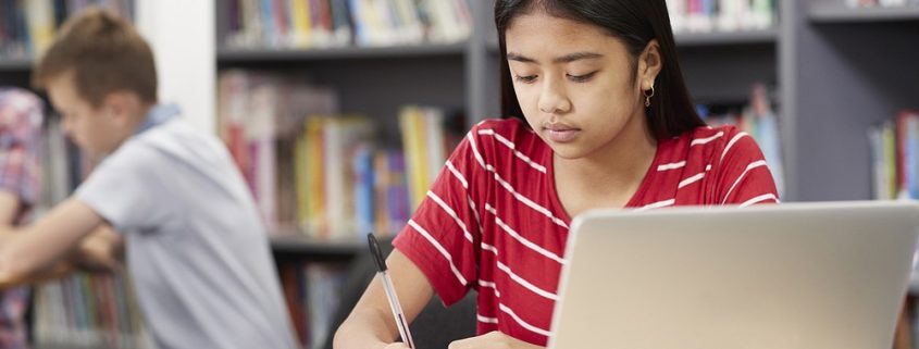 Female High School Student Working At Laptop In Library representing Benefit from Speech and Language Therapy