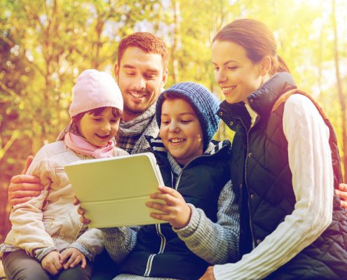 family in the woods smiling while looking at a tablet computer