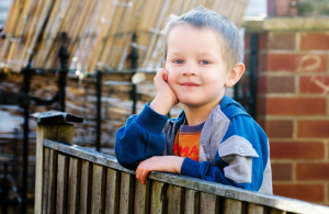 a child with his arm resting on a fence smiling at the camera