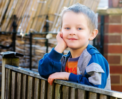 a child with his arm resting on a fence smiling at the camera