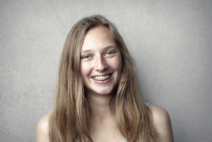 a girl with braces smiling at the camera with a grey background and long hair