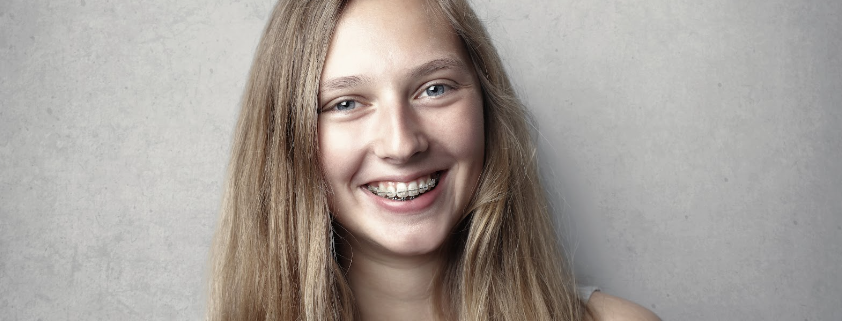 a girl with braces smiling at the camera with a grey background and long hair